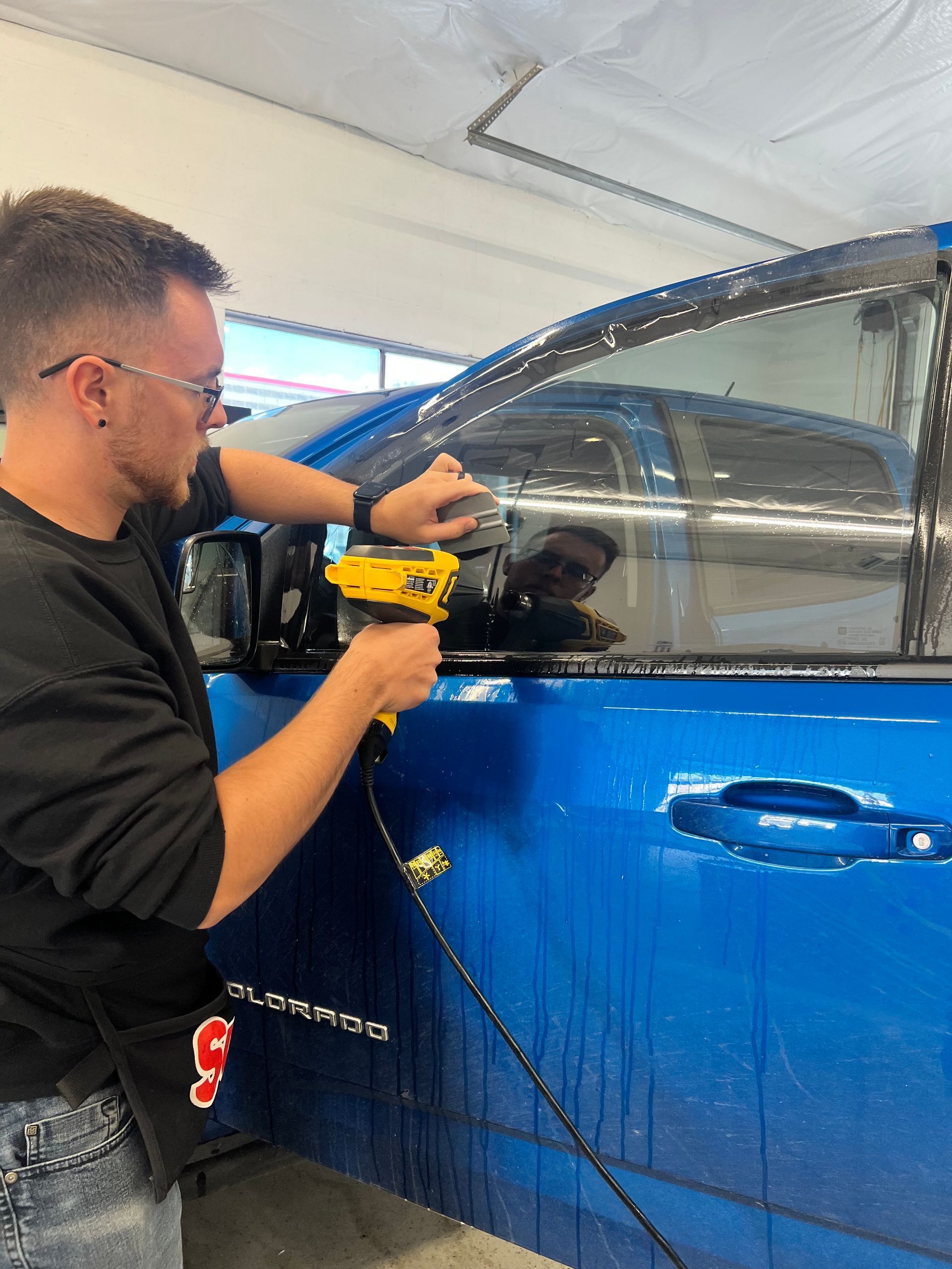 A man is working on a blue car with a drill.