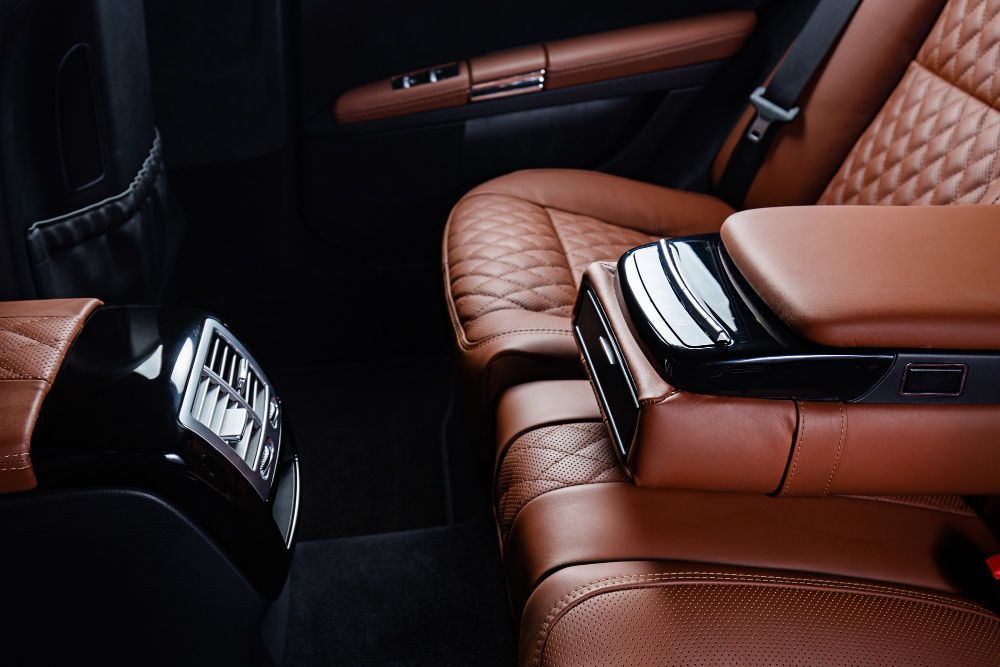 Brown leather car interior with quilted seats, armrest, and air vents.