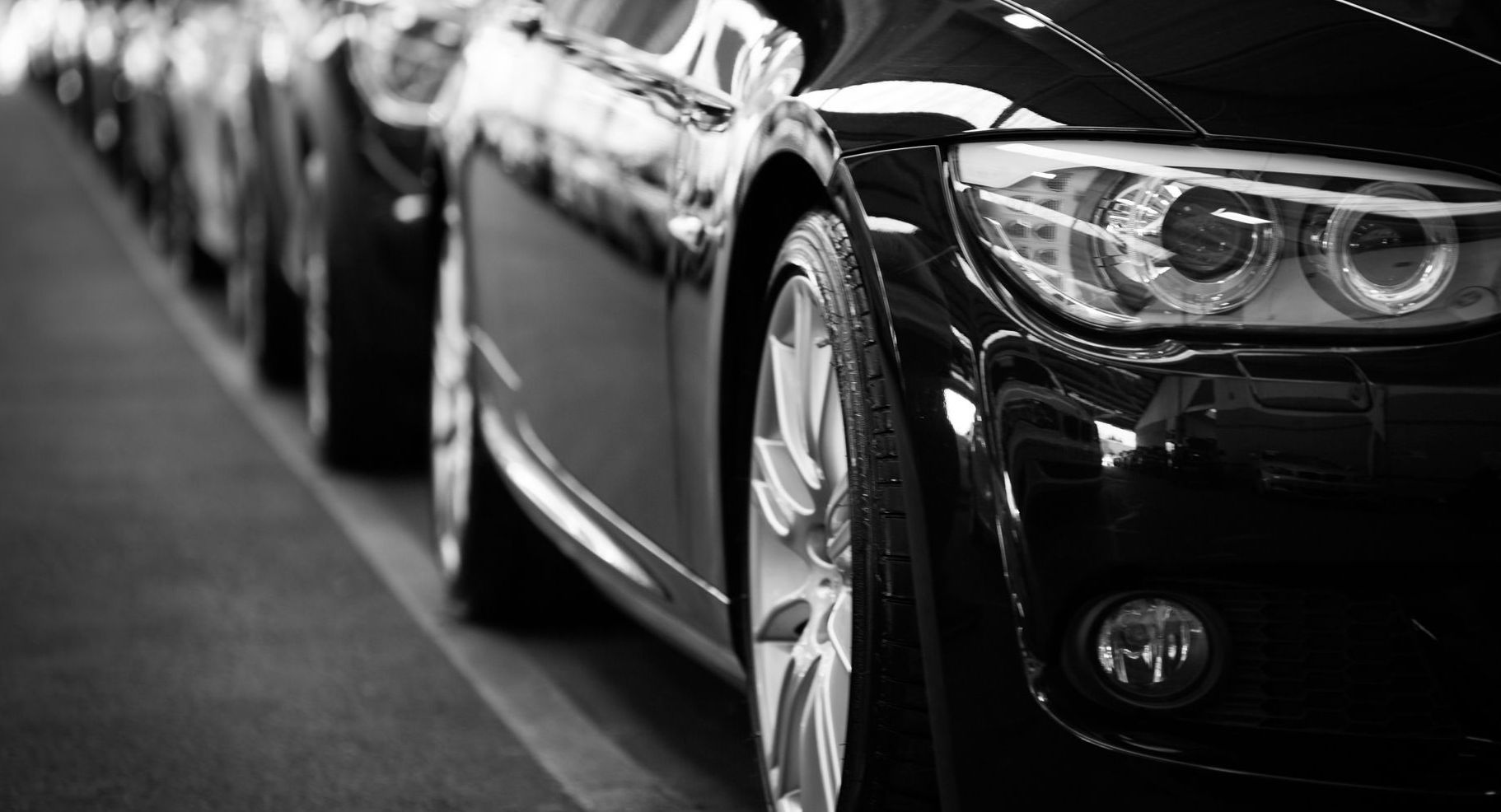 A black and white photo of a row of cars parked in a parking lot.