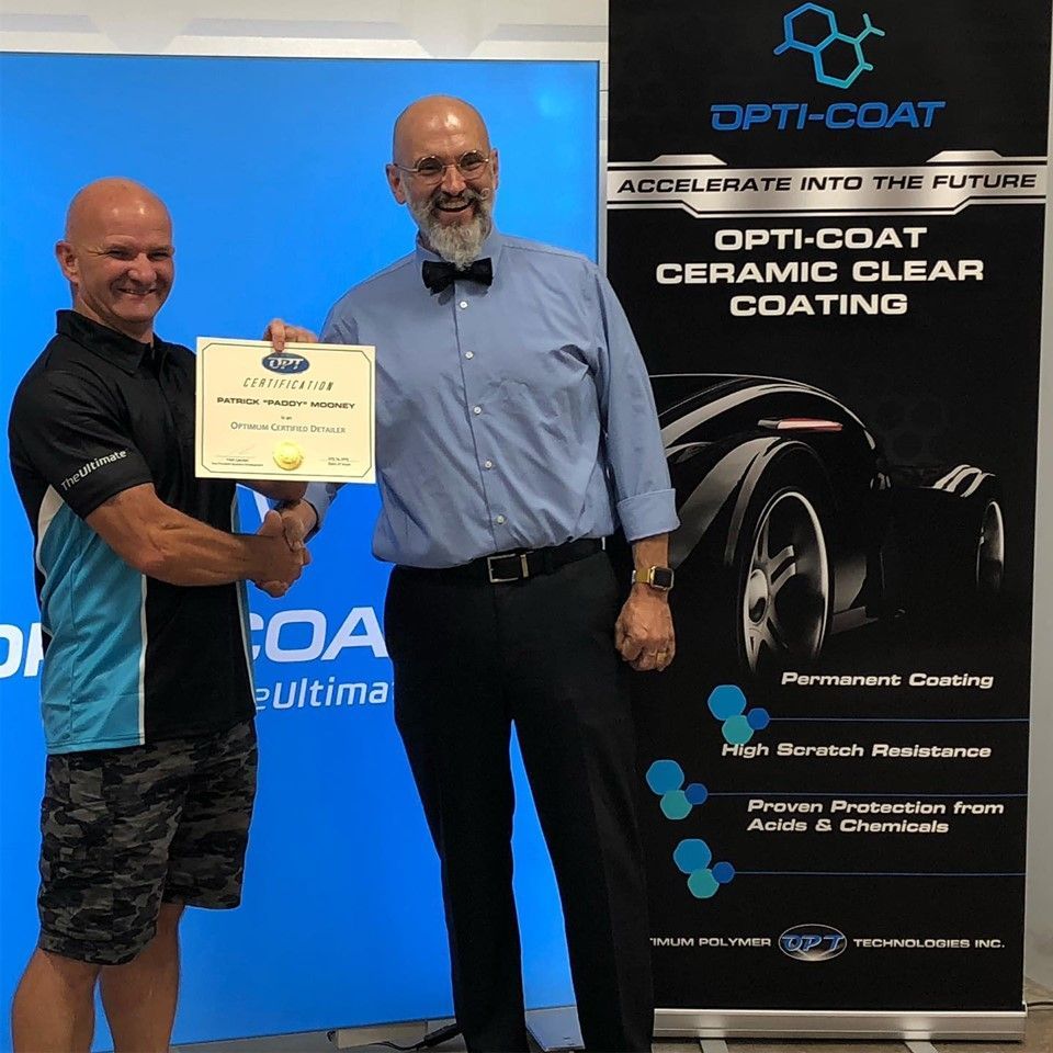 Two men shaking hands in front of a sign that says opti coat ceramic clear coating