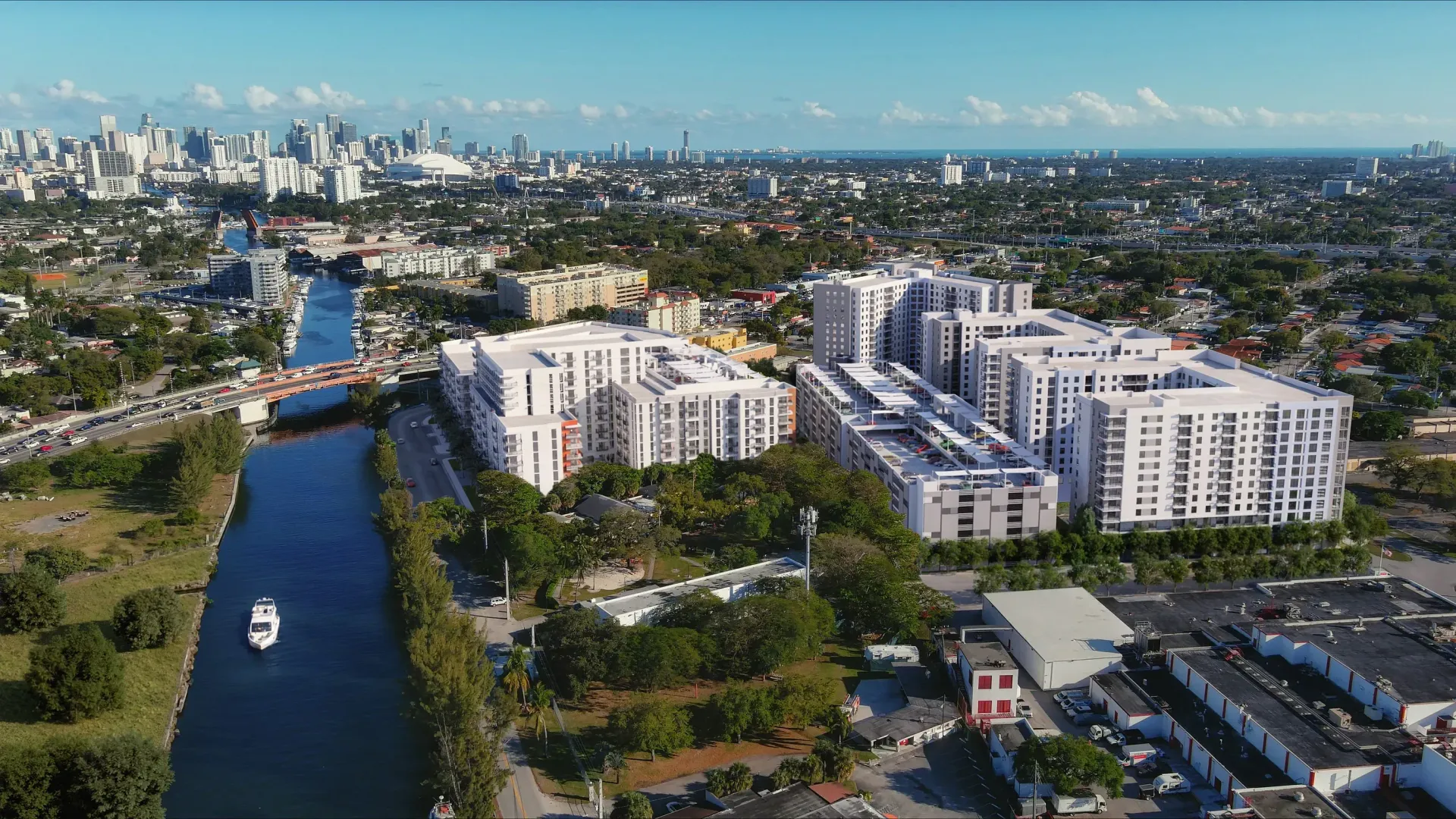 Aerial view of white apartment buildings beside a canal, with a city skyline in the distance