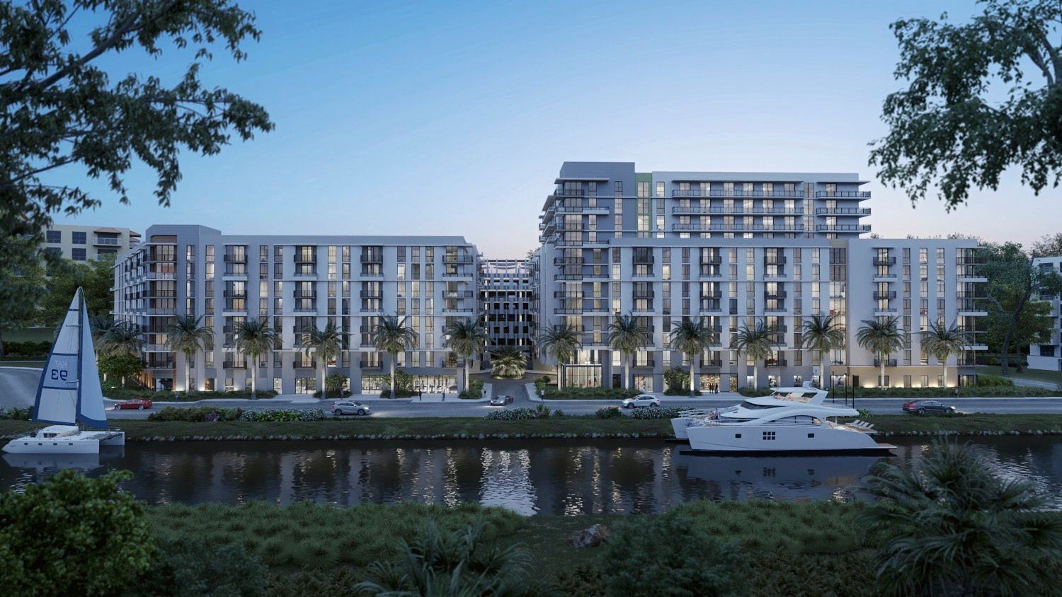 Waterfront modern apartment buildings at dusk with sailboat and yacht on calm river