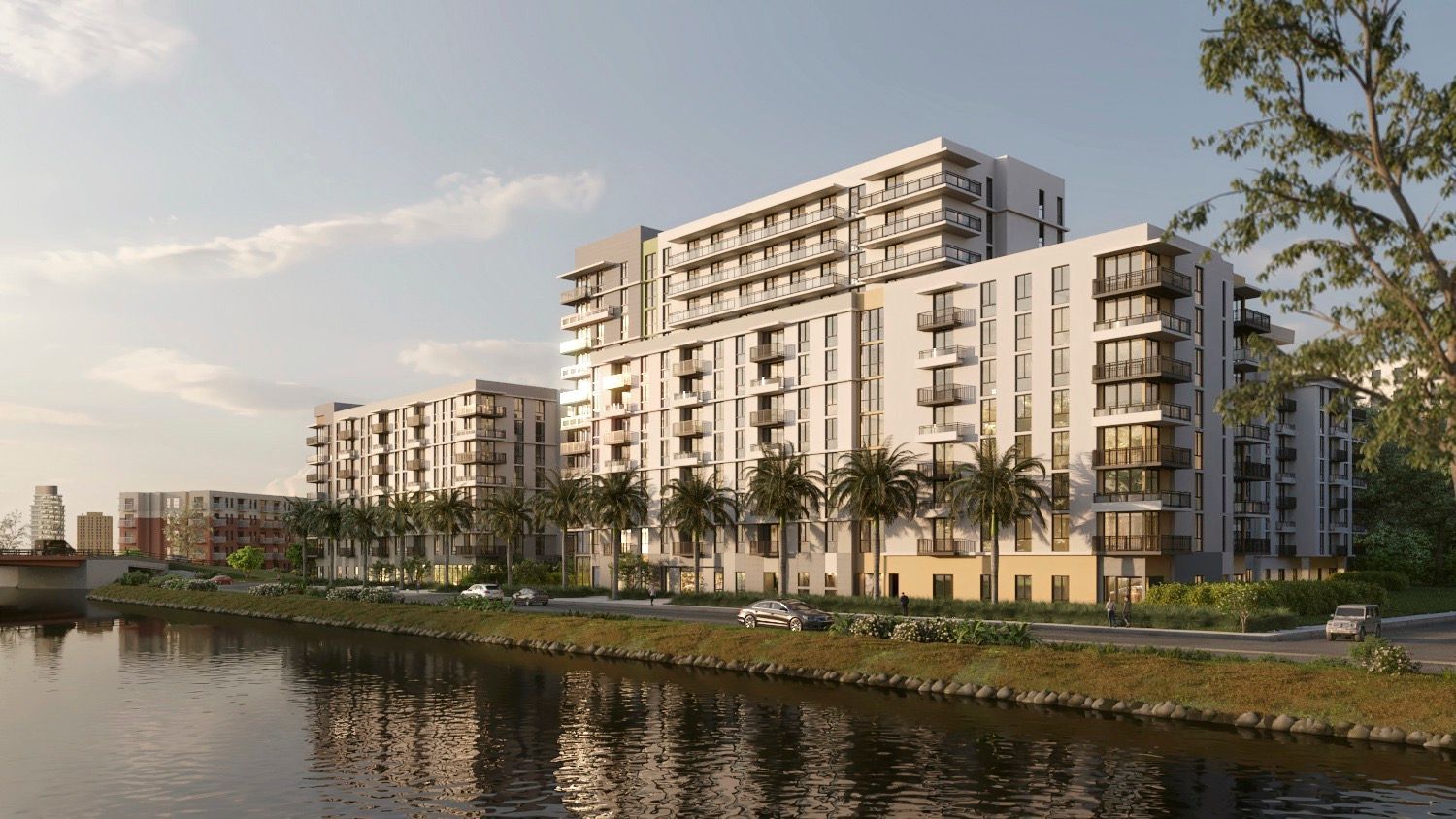Modern waterfront apartment buildings with balconies, reflected in calm water at sunset.
