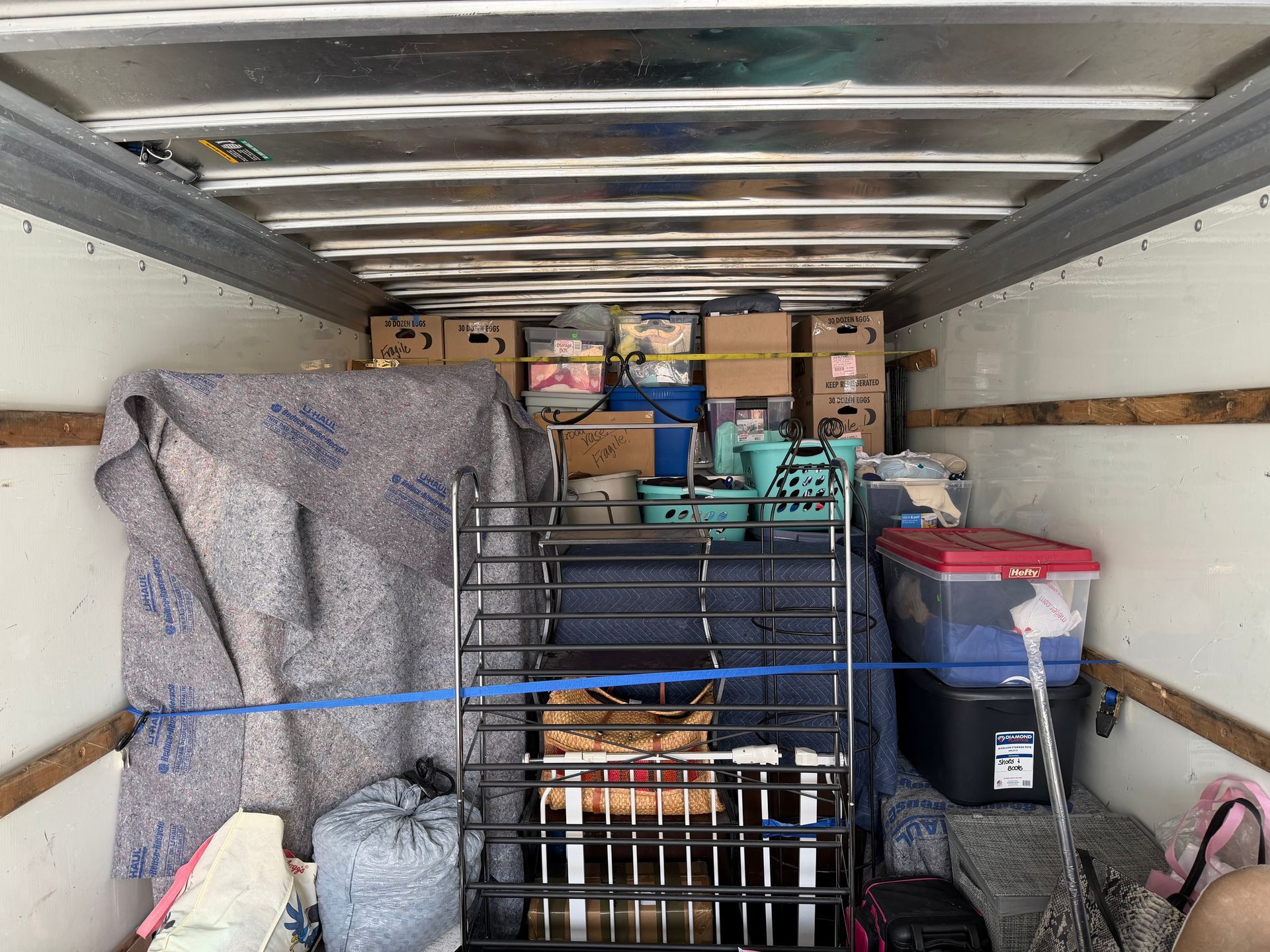Packed moving truck with stacked boxes, covered furniture, and storage bins secured inside.