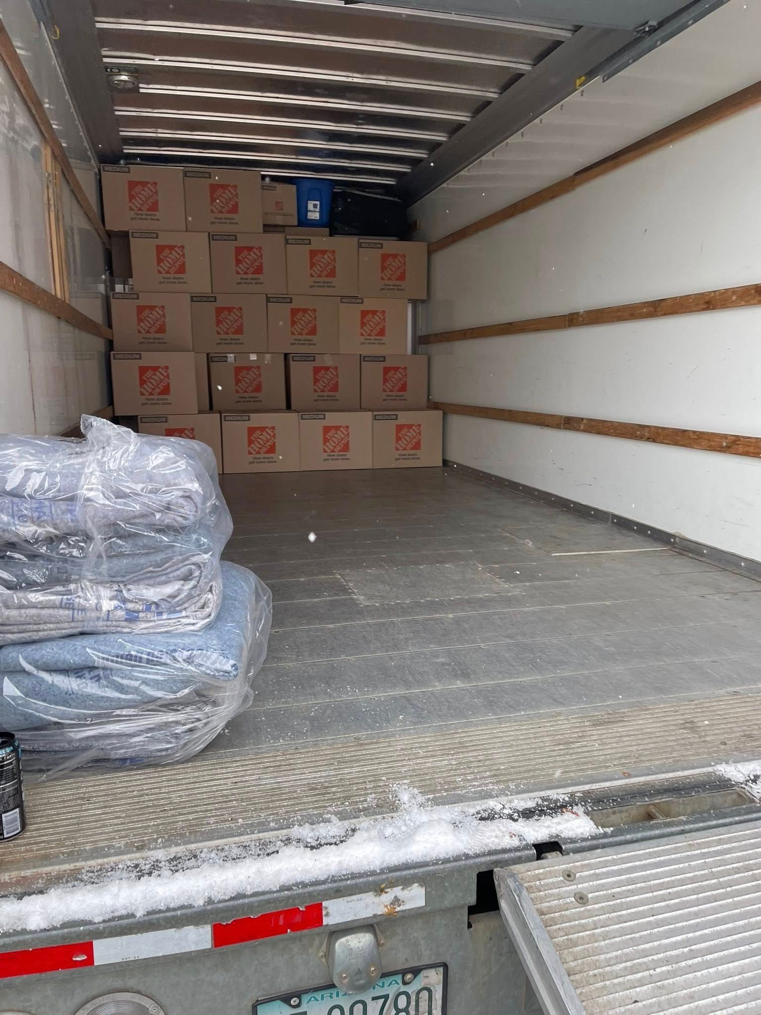 Empty moving truck with stacked boxes and wrapped furniture inside.