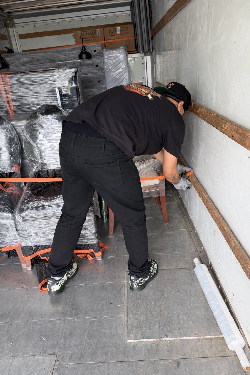 Worker bending over securing items inside a truck trailer amid packed cargo.