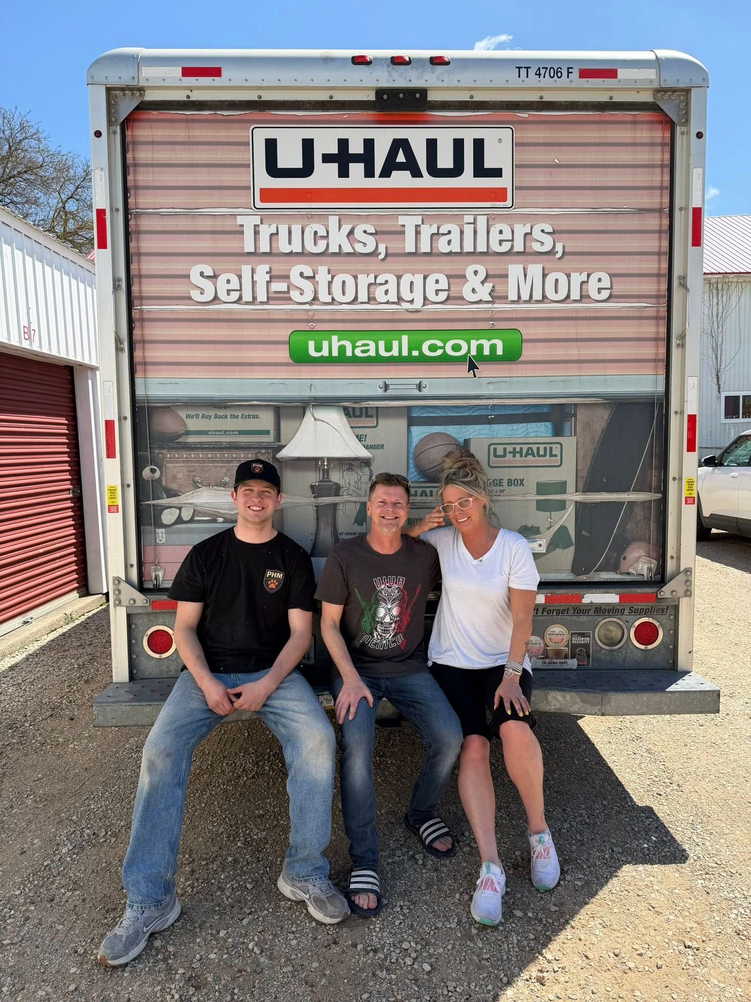 Three people sitting on the back of a U-Haul truck on a sunny day
