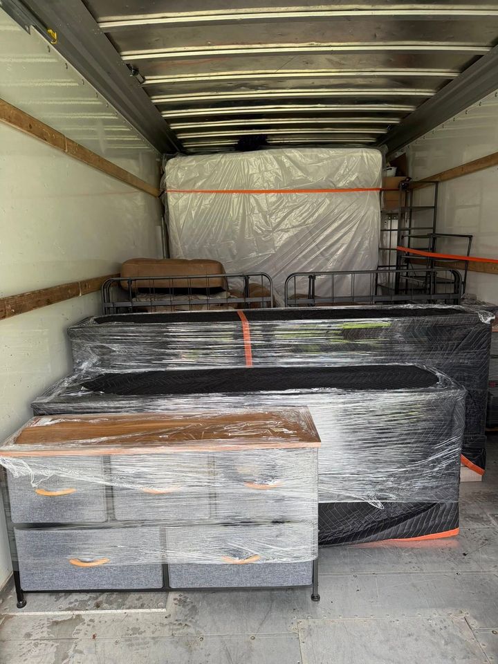 Truck trailer loaded with shrink-wrapped furniture and boxes, secured with orange straps
