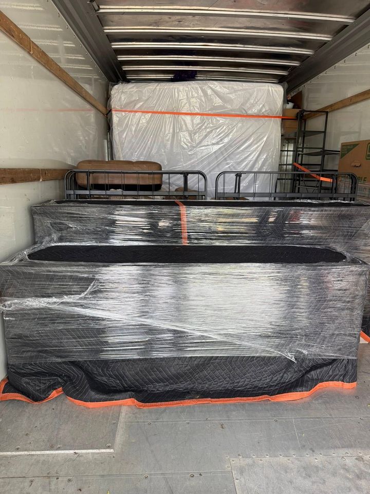 Loaded truck interior with wrapped cargo boxes and pallets secured by orange straps