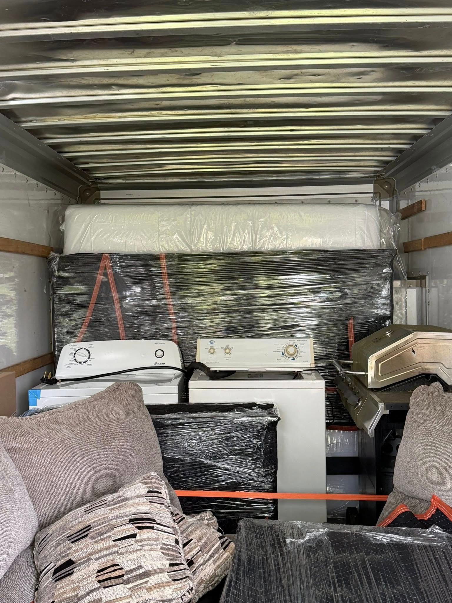 Packed moving truck with furniture, wrapped items, and boxes stacked inside.