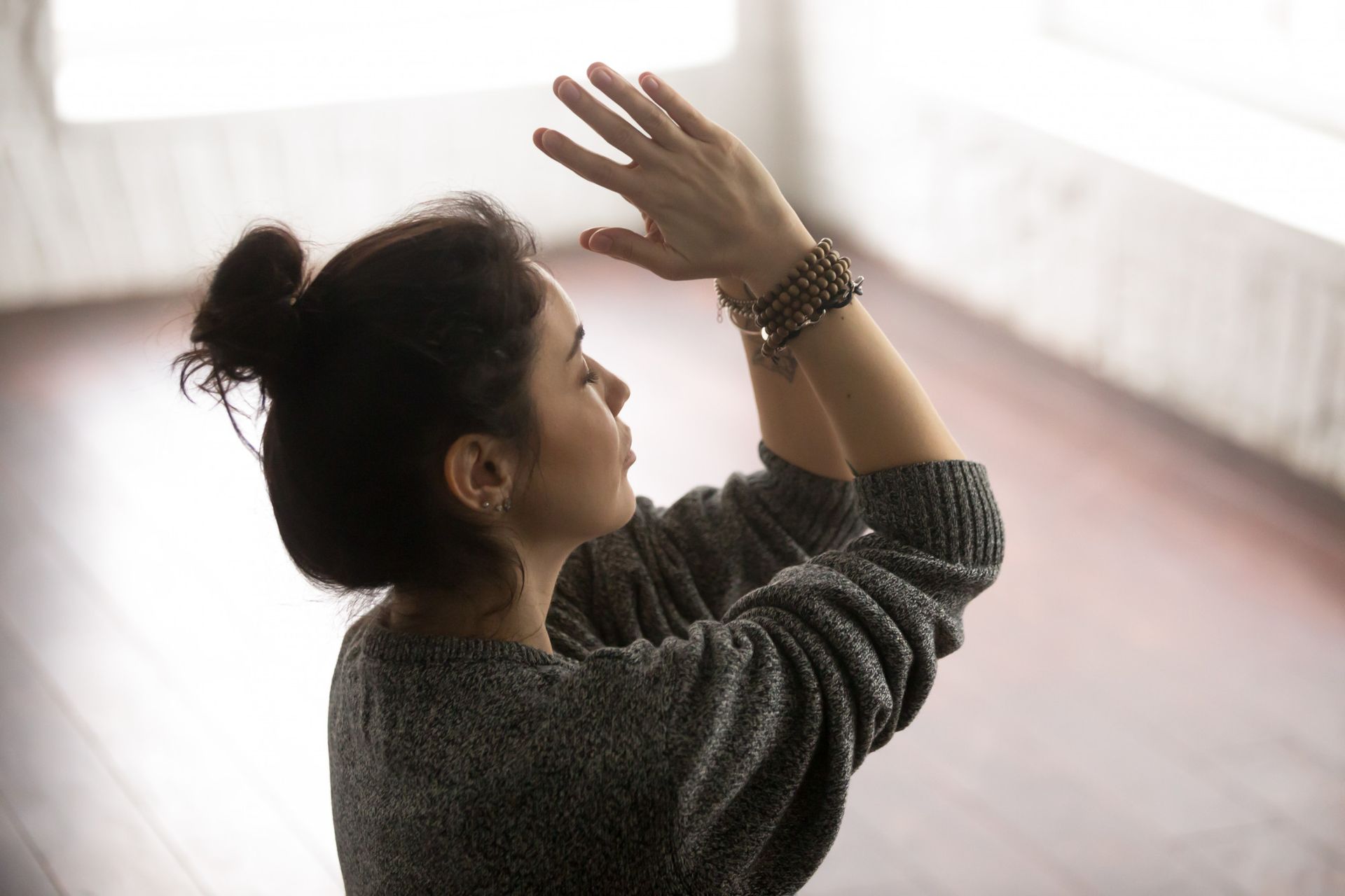 Mujer con suéter gris con las manos levantadas y los ojos cerrados.