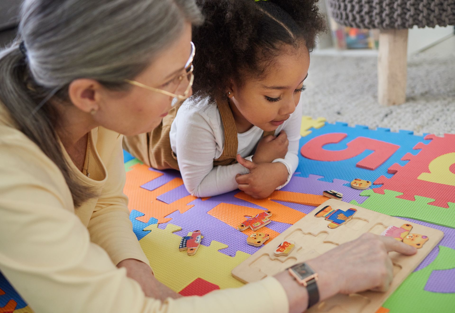 Adult and child playing with a puzzle on a colorful foam mat indoors