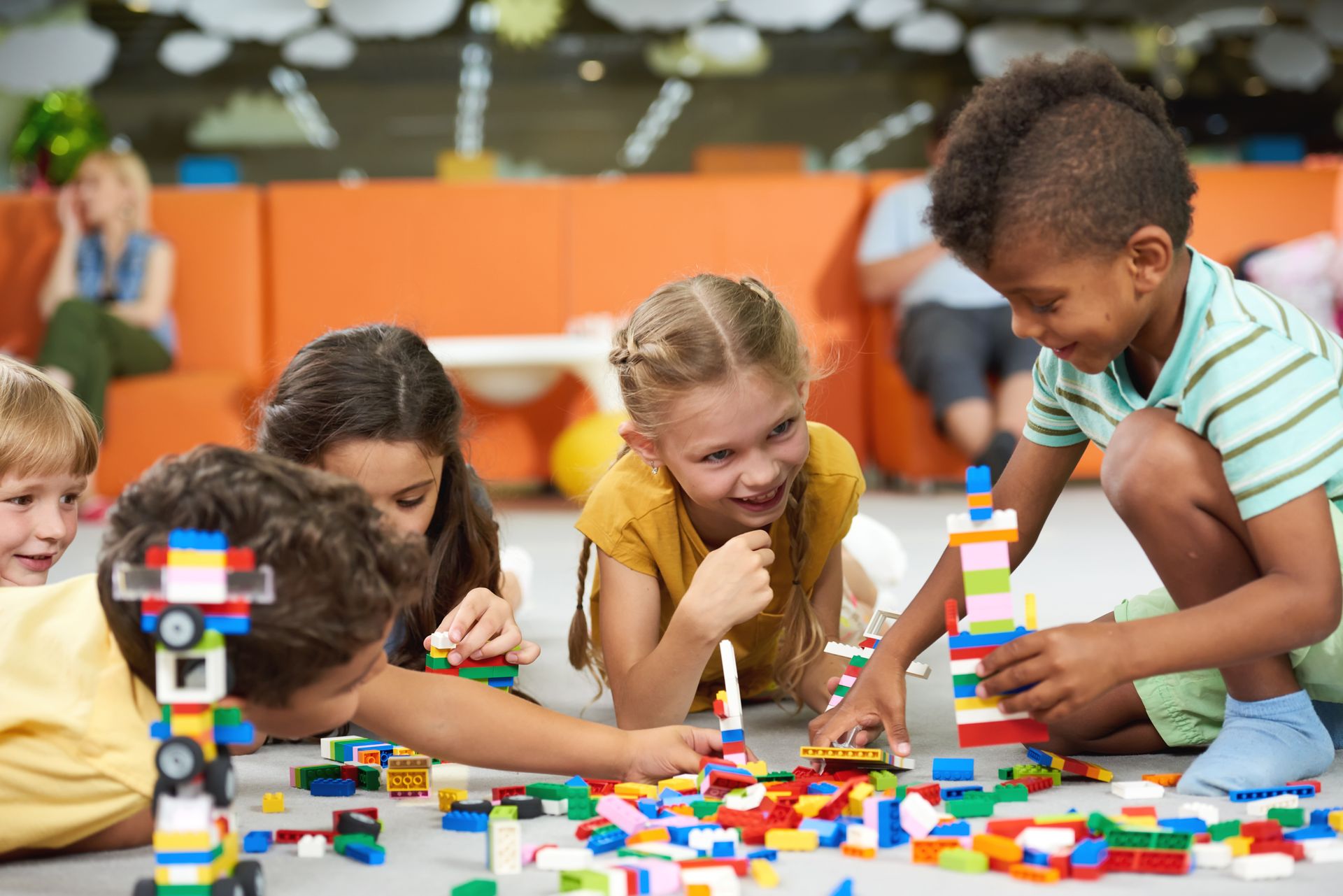 Showing a group of children with colorful LEGO bricks on a floor in a casual indoor setting.