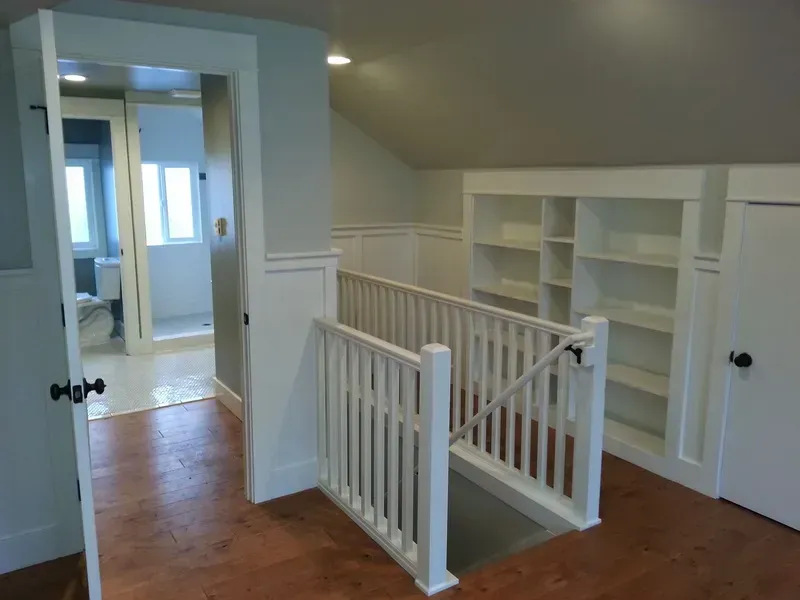 Interior of a room with a staircase, built-in shelves, and a doorway to a bathroom.