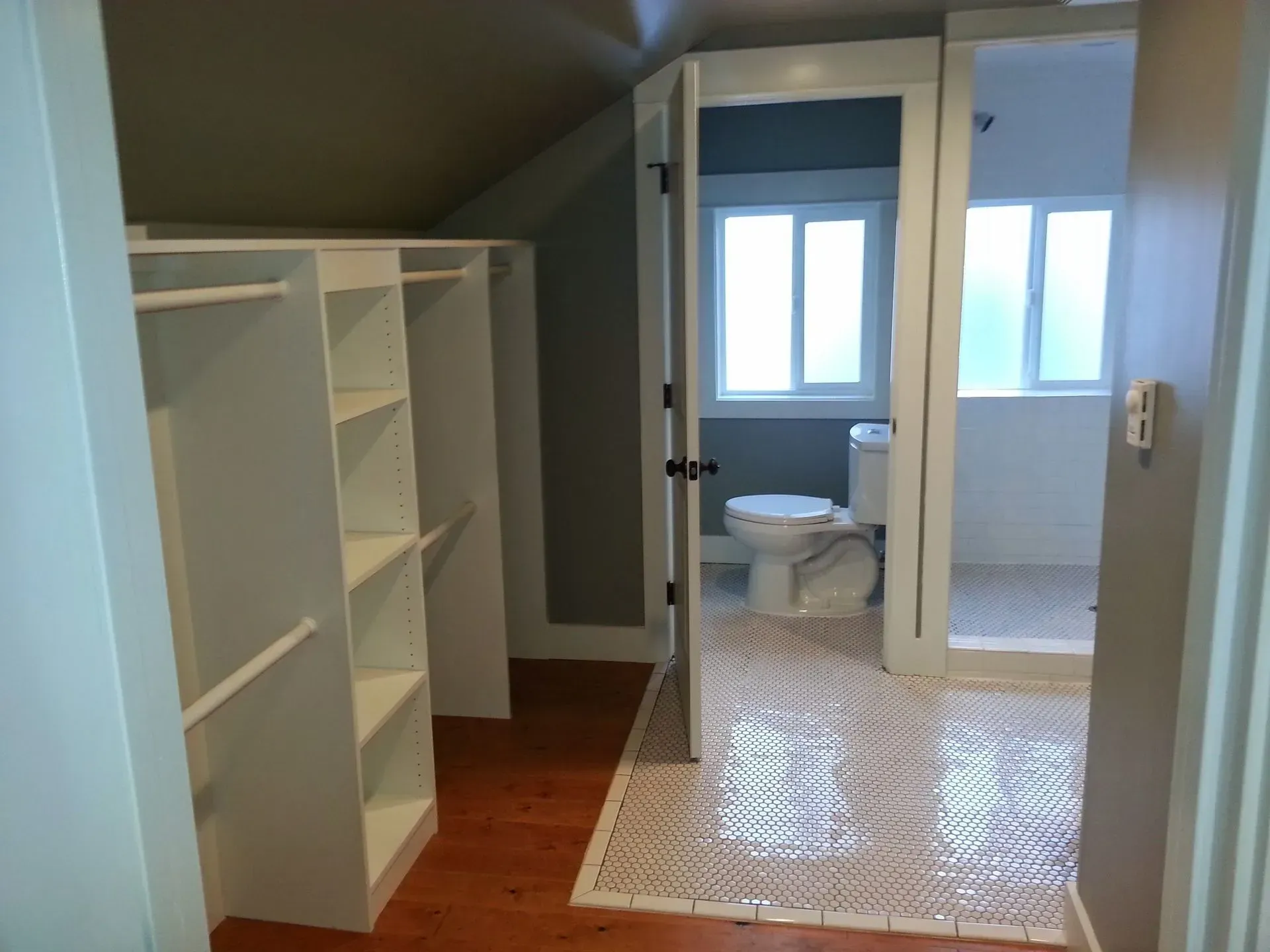 Walk-in closet with white shelving, open doorway to a bathroom with patterned tile and a toilet.