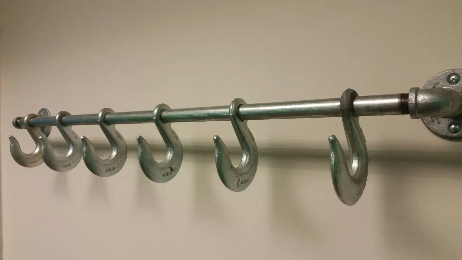 Metal hook rack on a wall with six large hooks.