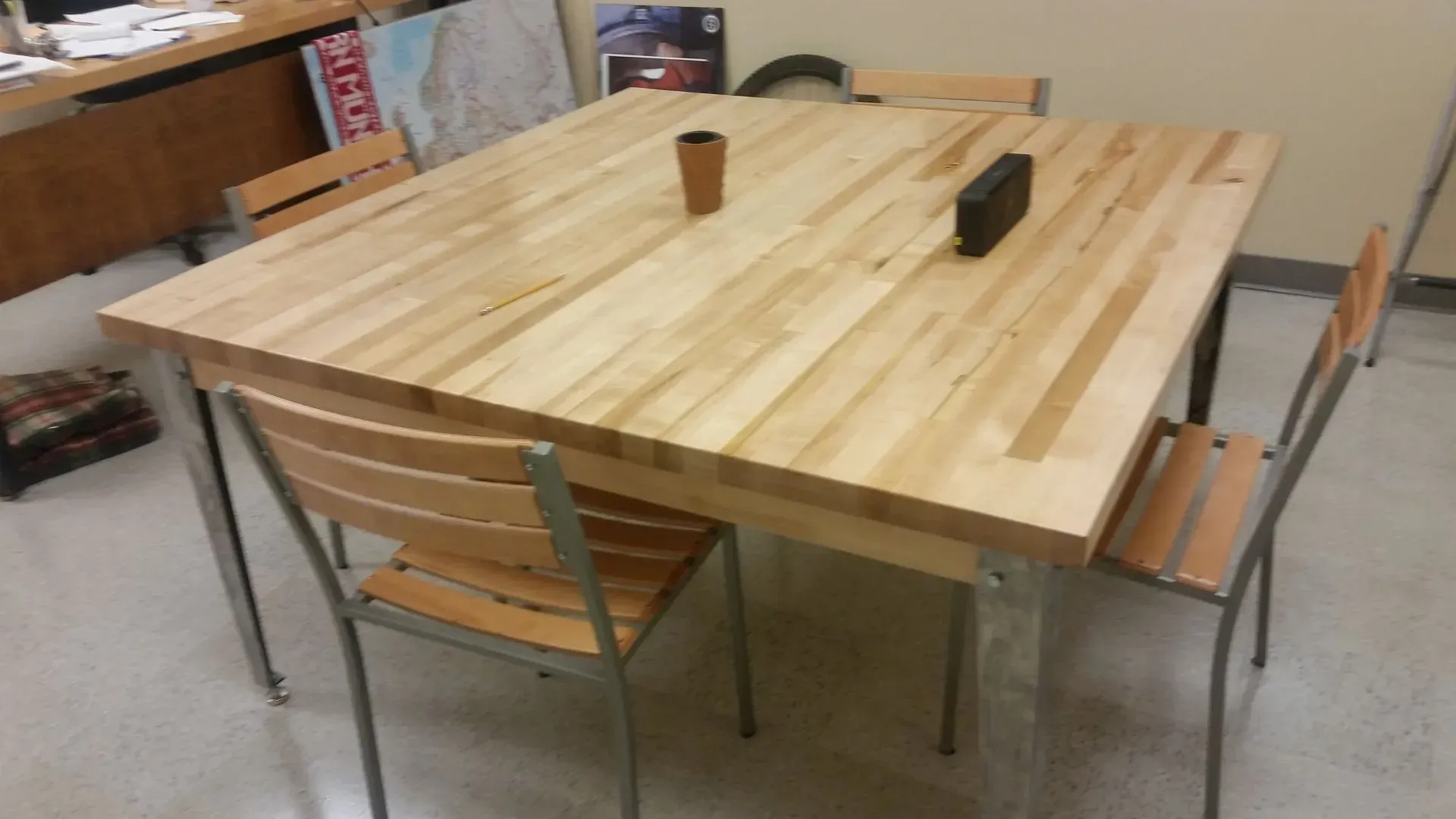 Wooden table with four chairs. A small vase and speaker sit on the table.