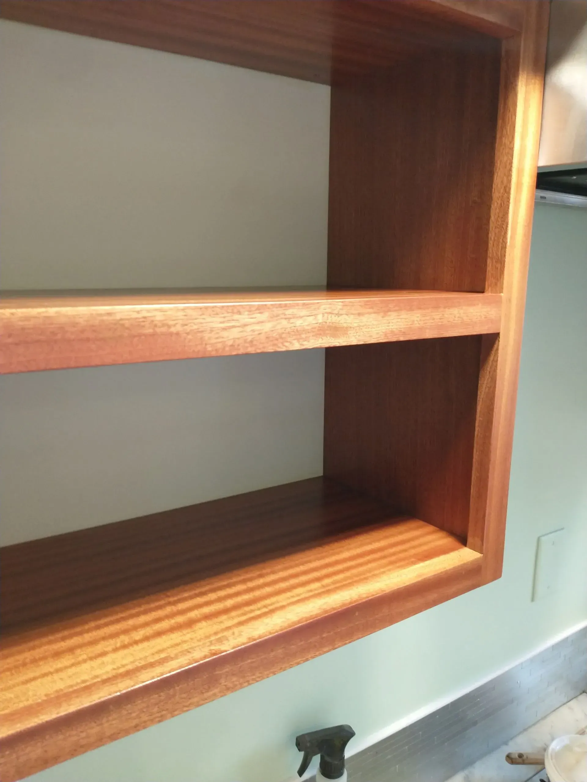 Wooden built-in shelving unit with two shelves. Brown wood against a white interior and a light green wall.