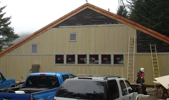Building under construction with yellow siding, windows, and roof, vehicles, and a ladder are present.
