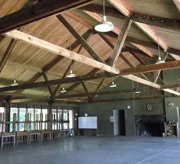 Interior of a wooden-beamed building with several overhead lights. Chairs are lined up near a glass wall.