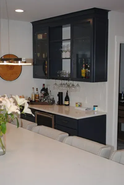 A built-in dark blue bar area with a wine fridge, cabinets, and glassware.