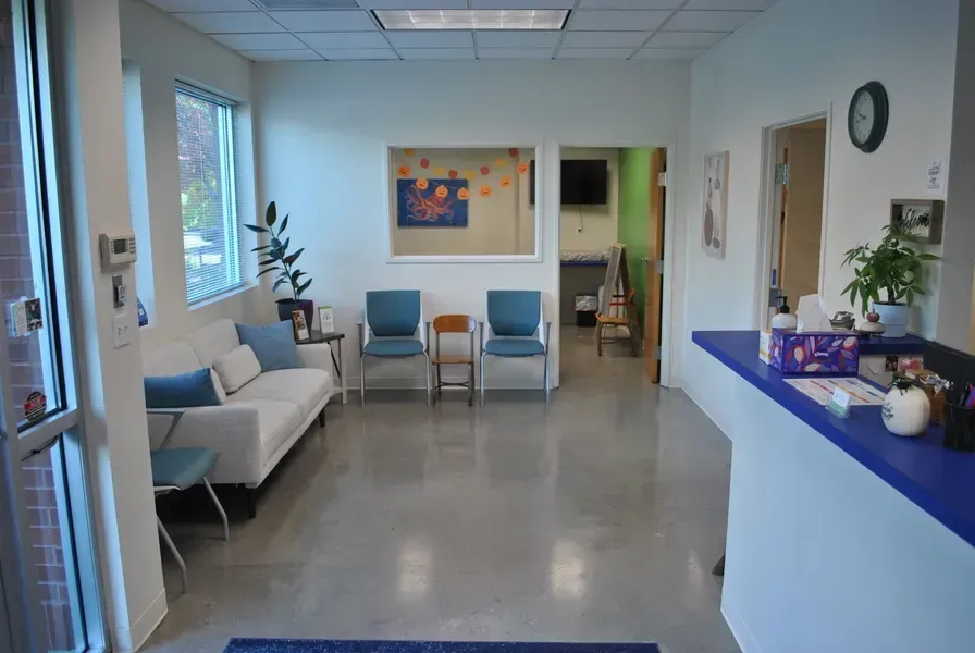 Waiting room with white sofa, blue chairs, and a reception desk.