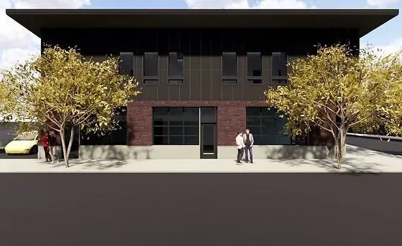Modern building facade with brick and dark panels. People stand in front. Trees frame the view.
