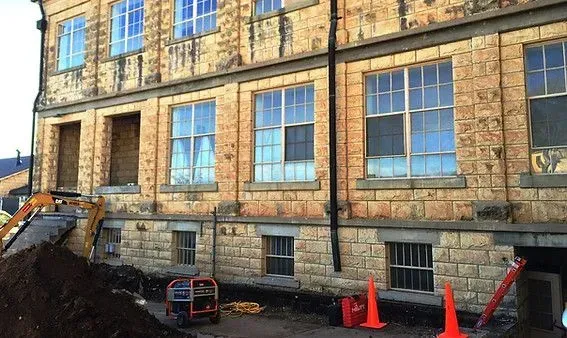Building exterior with stone facade, windows, and construction equipment.