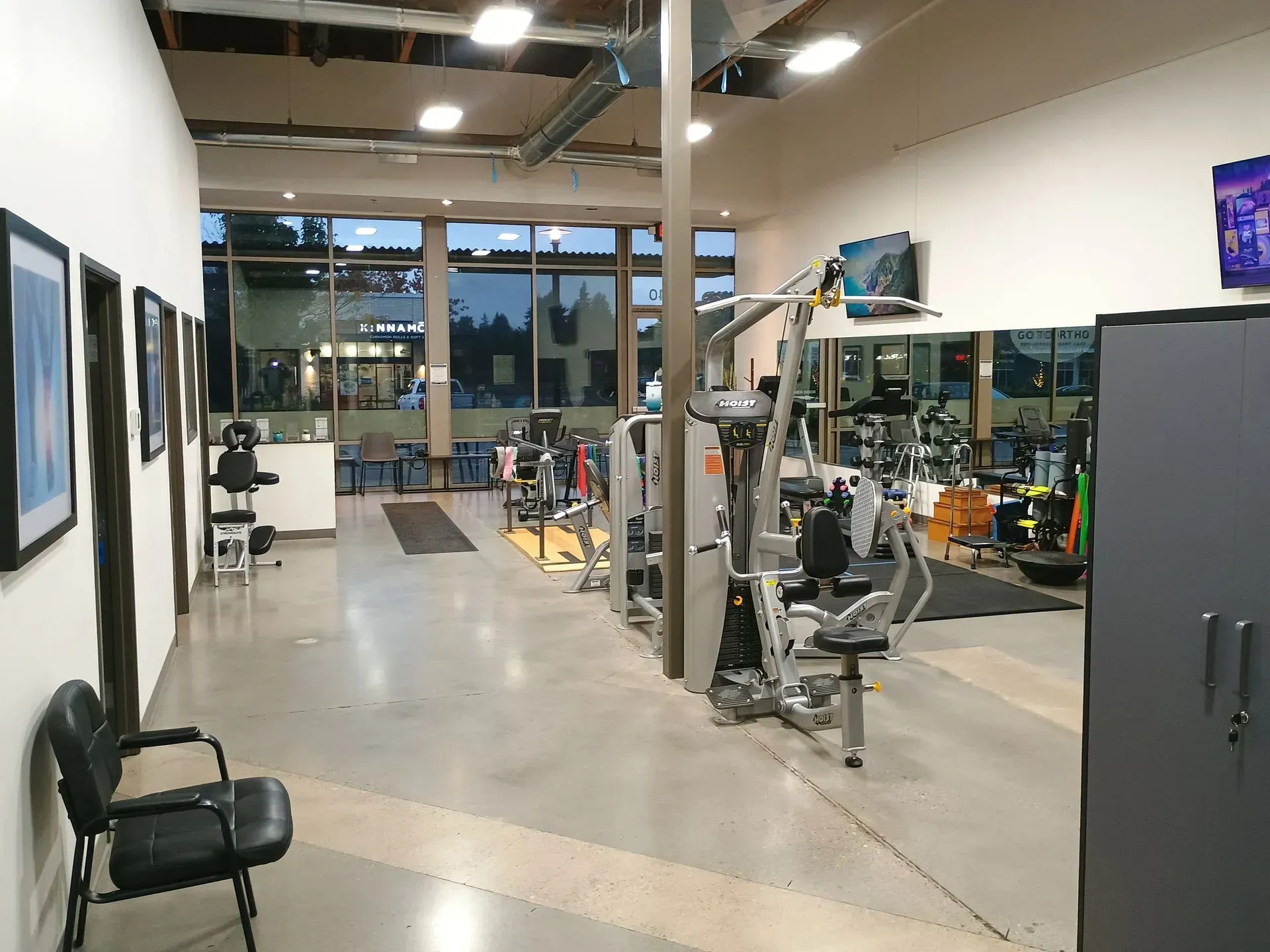 Gym interior with workout equipment, chairs, and windows.