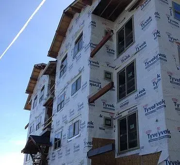 Building under construction with Tyvek wrap and exposed wooden beams. Windows are installed.