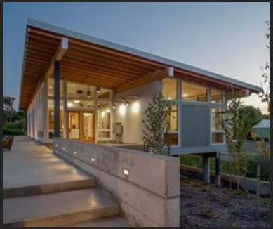 Modern two-story house with stone facade, lit porch, and landscaping at dusk.