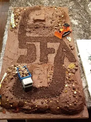Chocolate cake decorated as a construction site, with the letters "SFJ" in frosting and toy trucks.