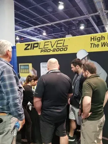 People at a trade show booth for the ZIPLEVEL PRO-2000. Display shows device with others examining it.