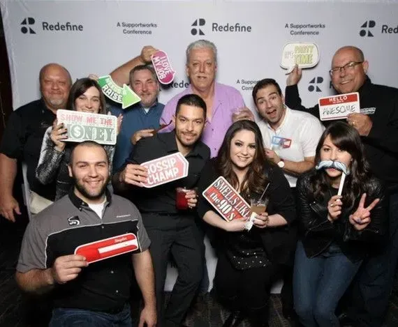 Group of people posing with props at an event with a backdrop that has Redefine branding.