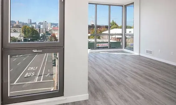 Empty room with gray wood-look flooring, large windows, and a city view.