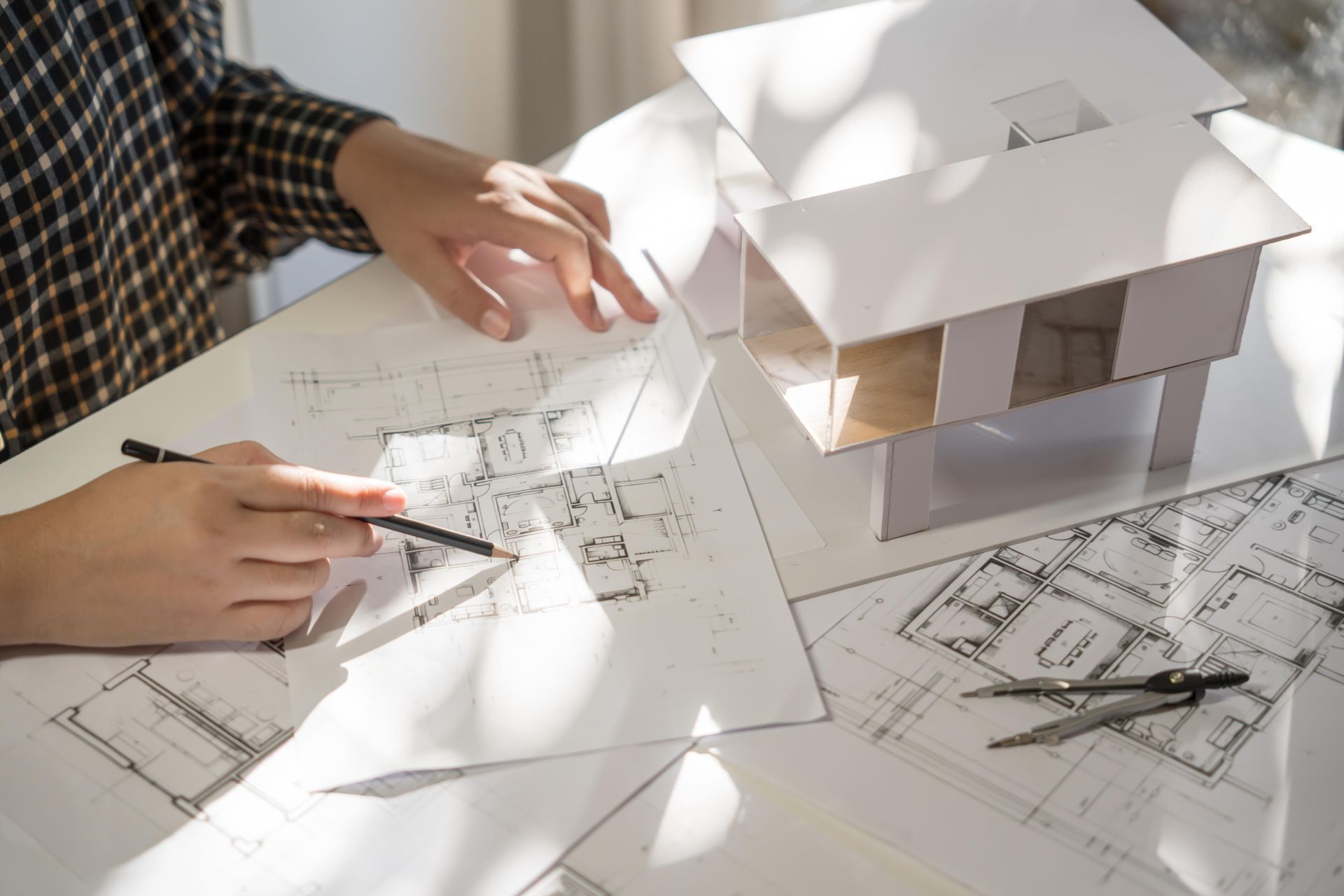 Architect at work, drawing plans with a pencil; model home and tools on the table.