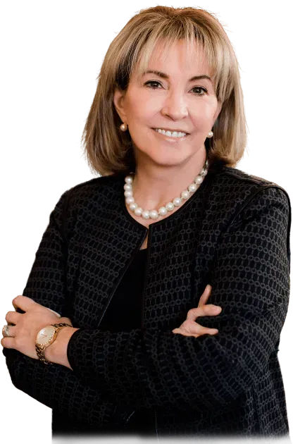 Woman in black jacket, pearl necklace, arms crossed, smiling, studio setting.