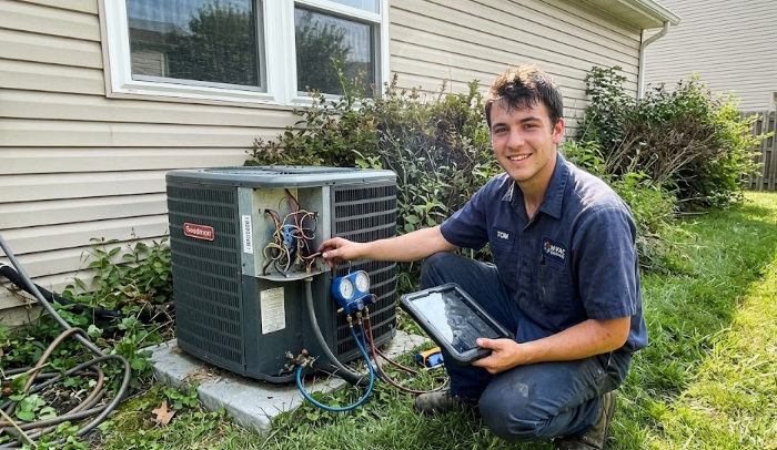 A friendly Spokane Heating and Cooling technician smiling next to a newly installed residential air conditioning unit.
