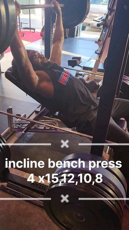 Man performing incline bench press at the gym; lifting a barbell; workout routine.