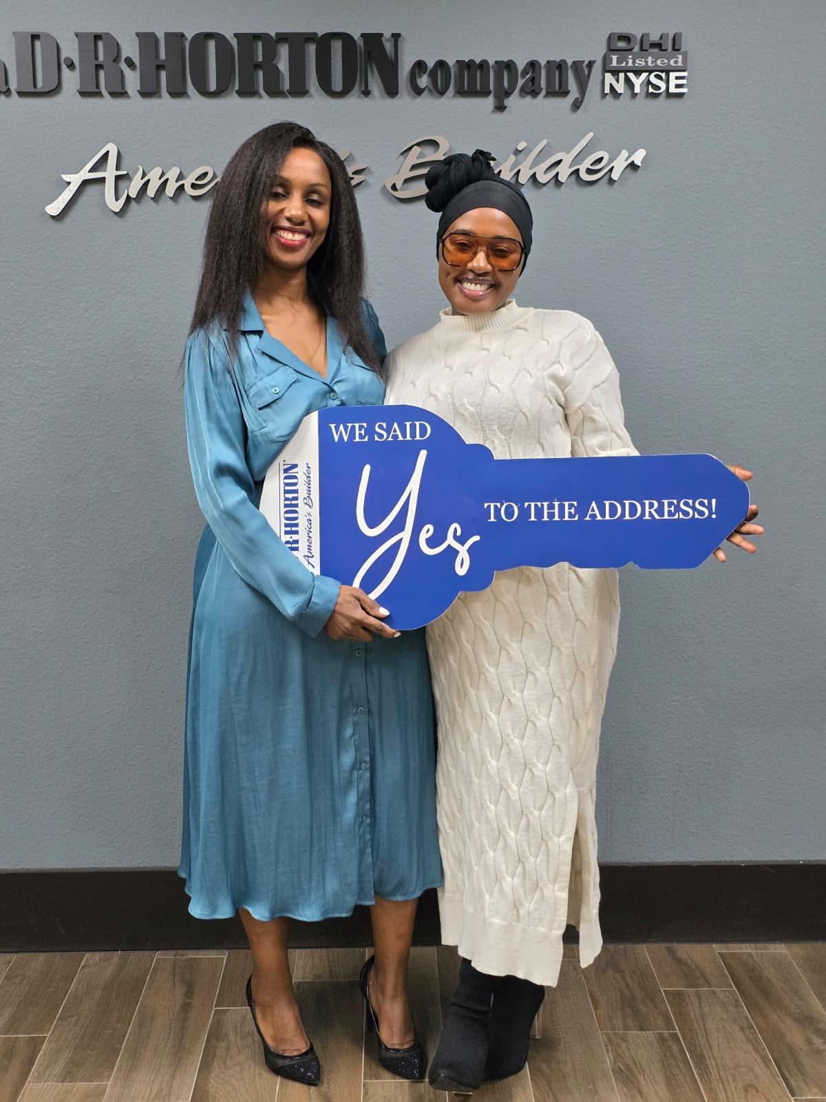 Two women holding a blue “We said Yes to the address!” sign at a company event backdrop