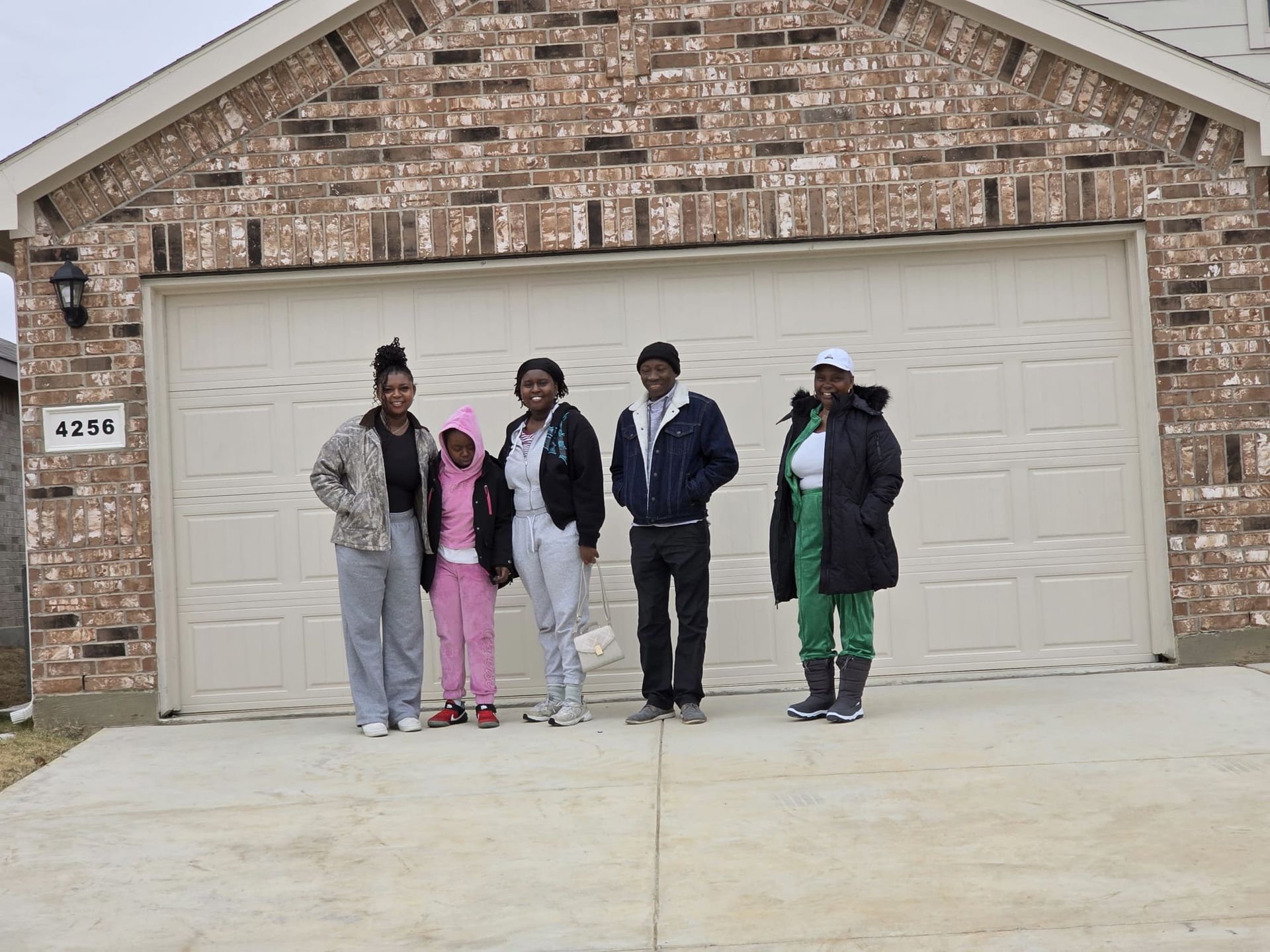 Five people standing in front of a brick house and white garage door