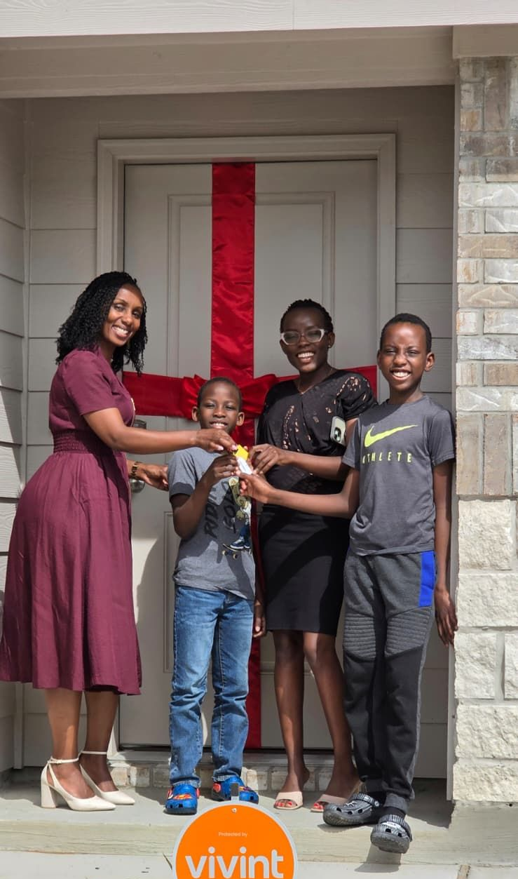 Five people standing on a front porch, smiling and holding a colorful bouquet, with a red door behind them
