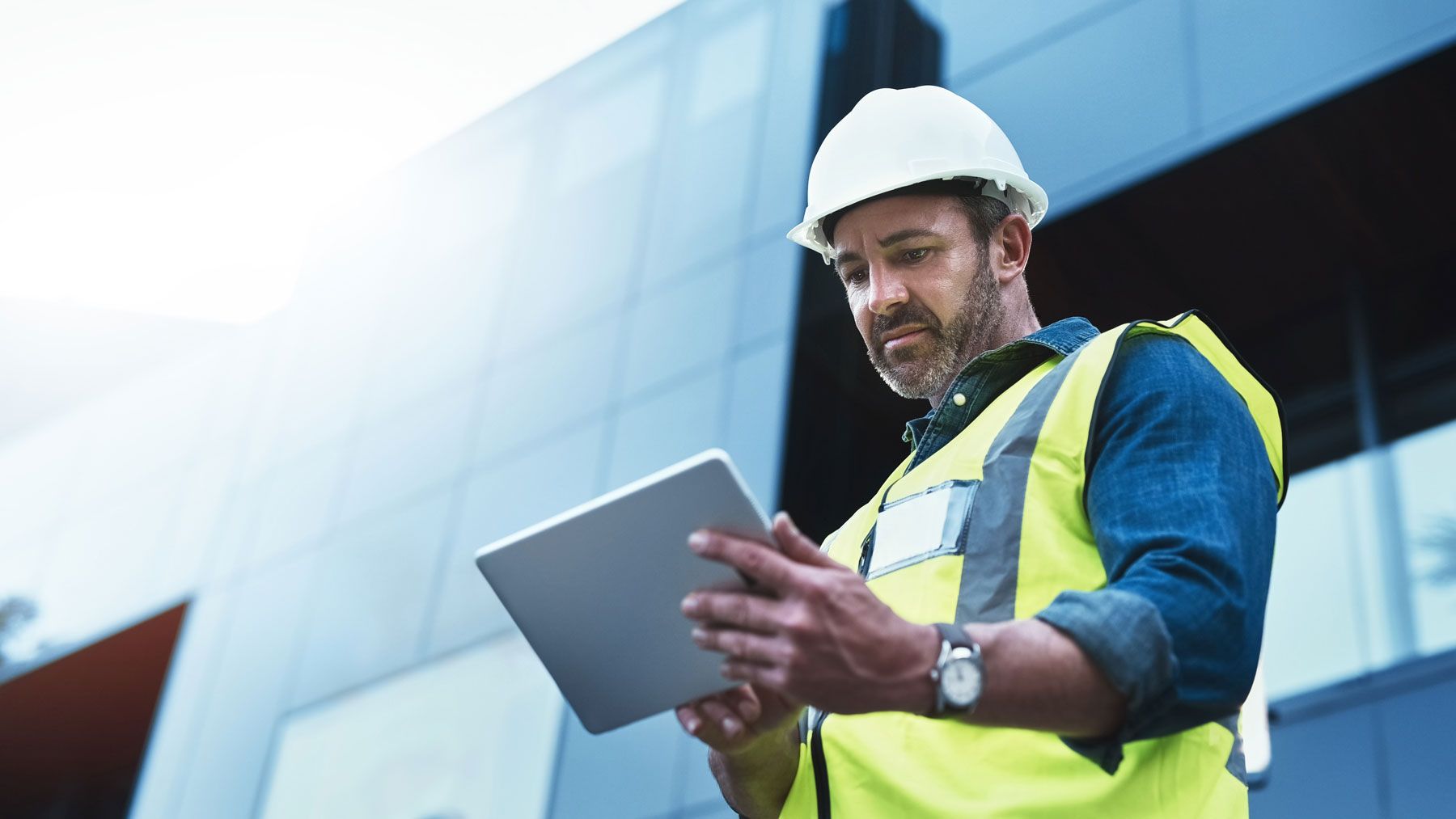 Construction manager wearing a hard hat and safety vest using a tablet to manage payroll records at