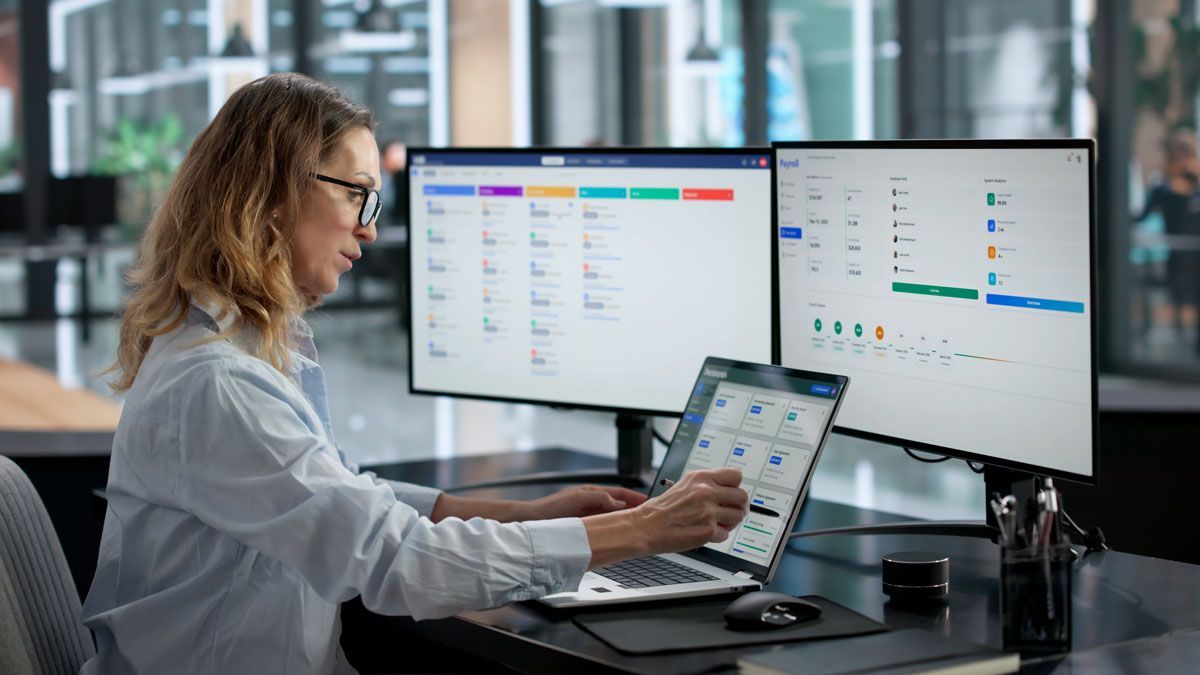 Payroll specialist managing employee payroll and tax information on multiple screens