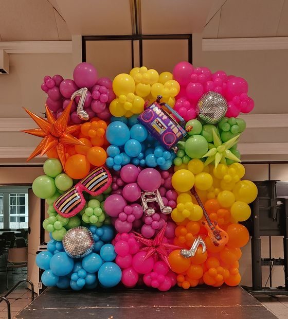 Colorful balloon wall display with pink, yellow, blue, green, orange, and silver balloons arranged in a square