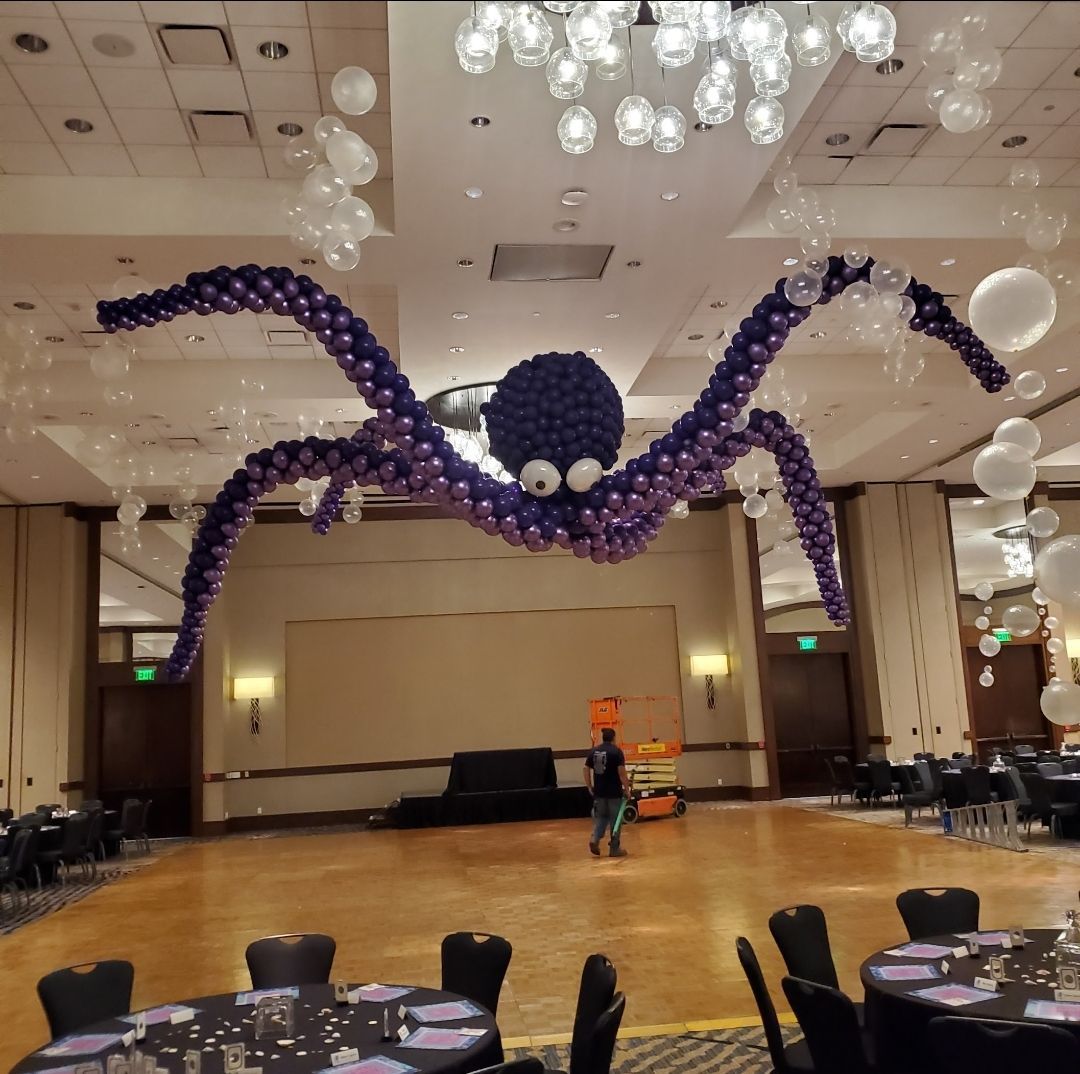 Purple balloon octopus hanging over a ballroom dance floor with chandeliers and tables nearby