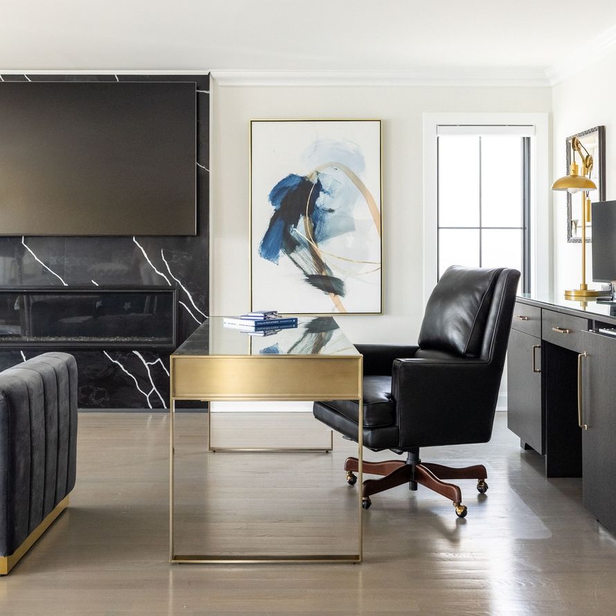 Modern home office: black leather chair, gold desk, abstract art, fireplace, built-in desk.
