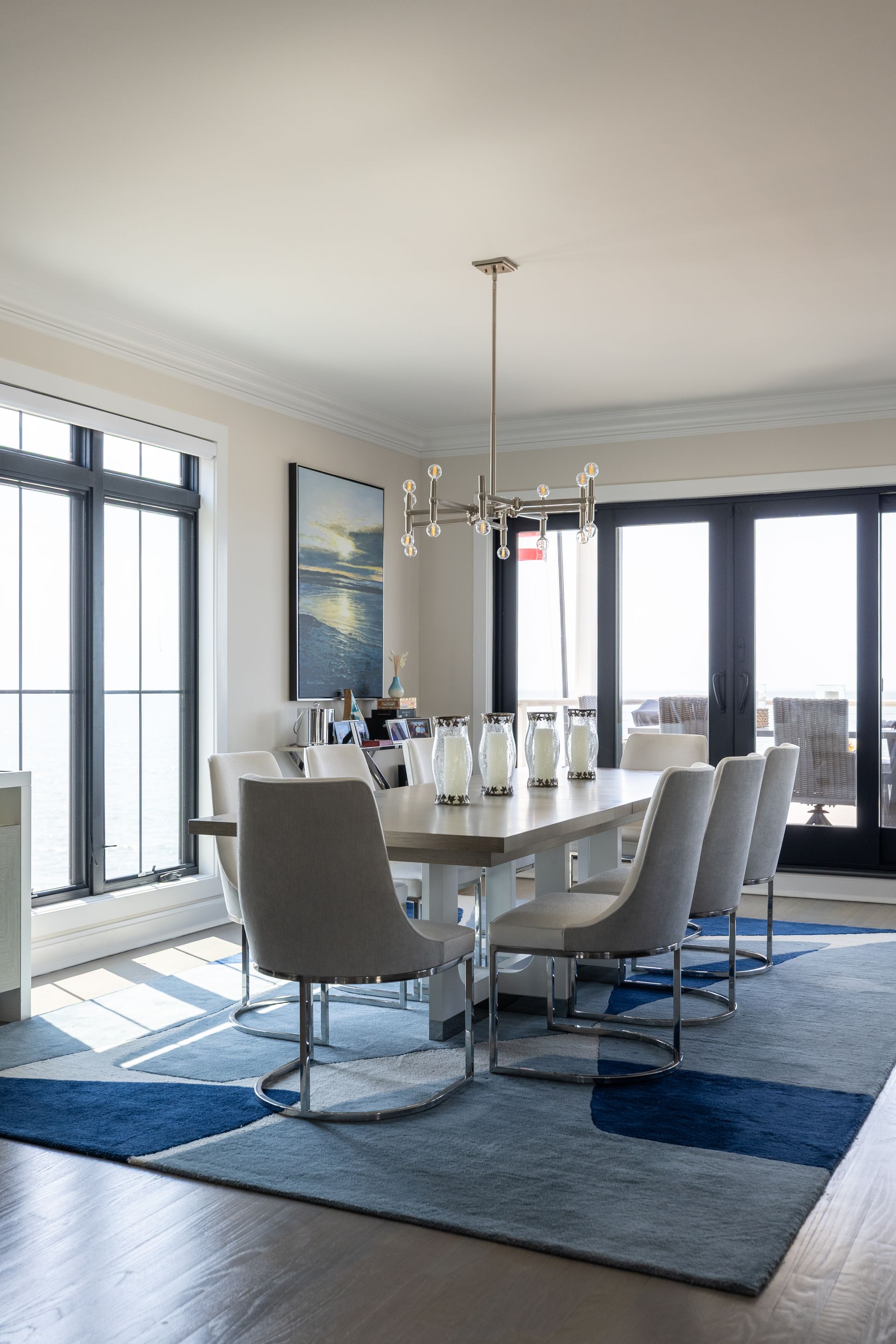 Dining room with large windows, modern table and chairs, blue geometric rug.