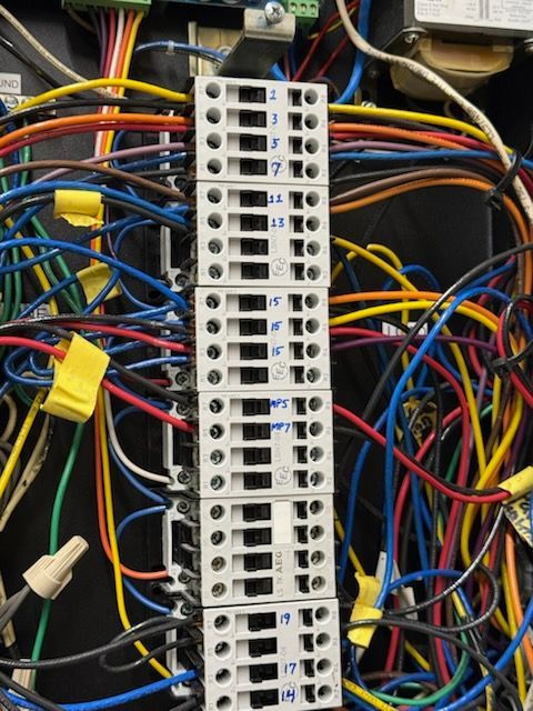 A vertical terminal block in a wiring cabinet with many multicolored electrical wires connected to its numbered points.