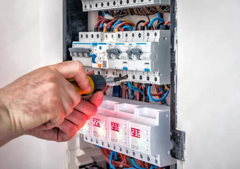 A close-up of a hand using a screwdriver to tighten a terminal screw on an electrical circuit breaker panel.